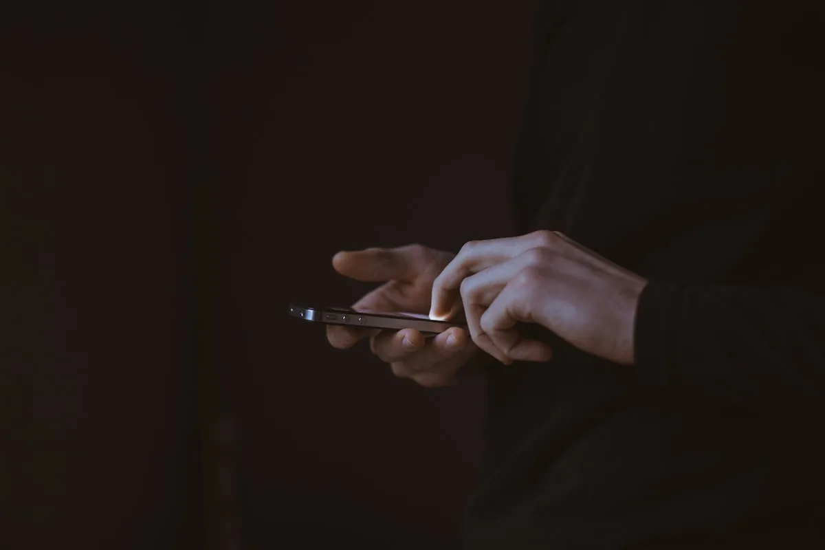 Personne tenant un smartphone dans le noir, représentant le jeu mobile basé sur navigateur chez WinLion Casino